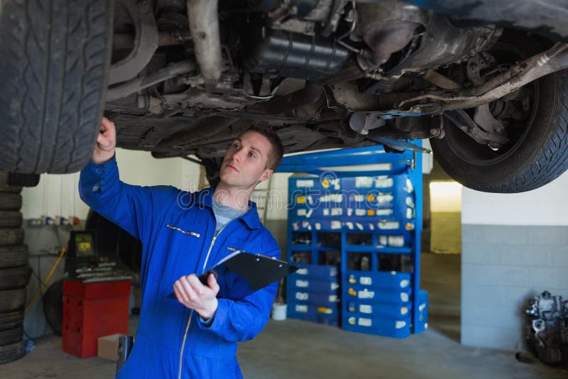 Mechanic in a real garage inspecting the undercarriage of a vehicle on a lift, showing the kind of specialized work that drives up repair costs and electric vehicle insurance premiums