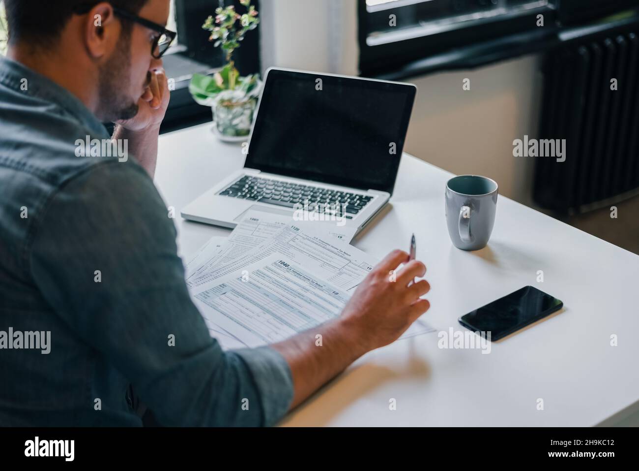 A person thoughtfully filling out IRS tax forms at a desk with a laptop, preparing to claim the remaining federal EV tax credit in 2026