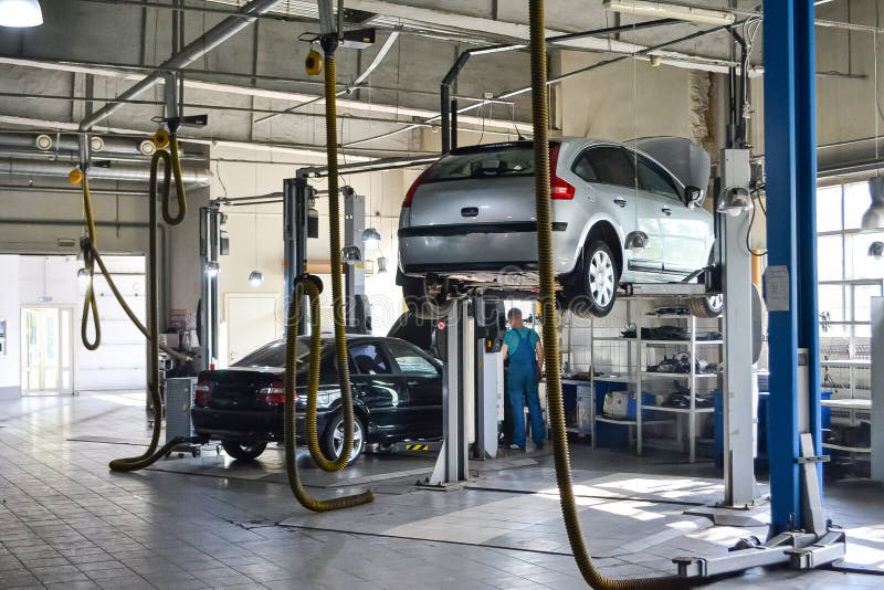 Two cars side by side in a repair shop, one on a lift, illustrating the comparison of maintenance needs between traditional and electric vehicles