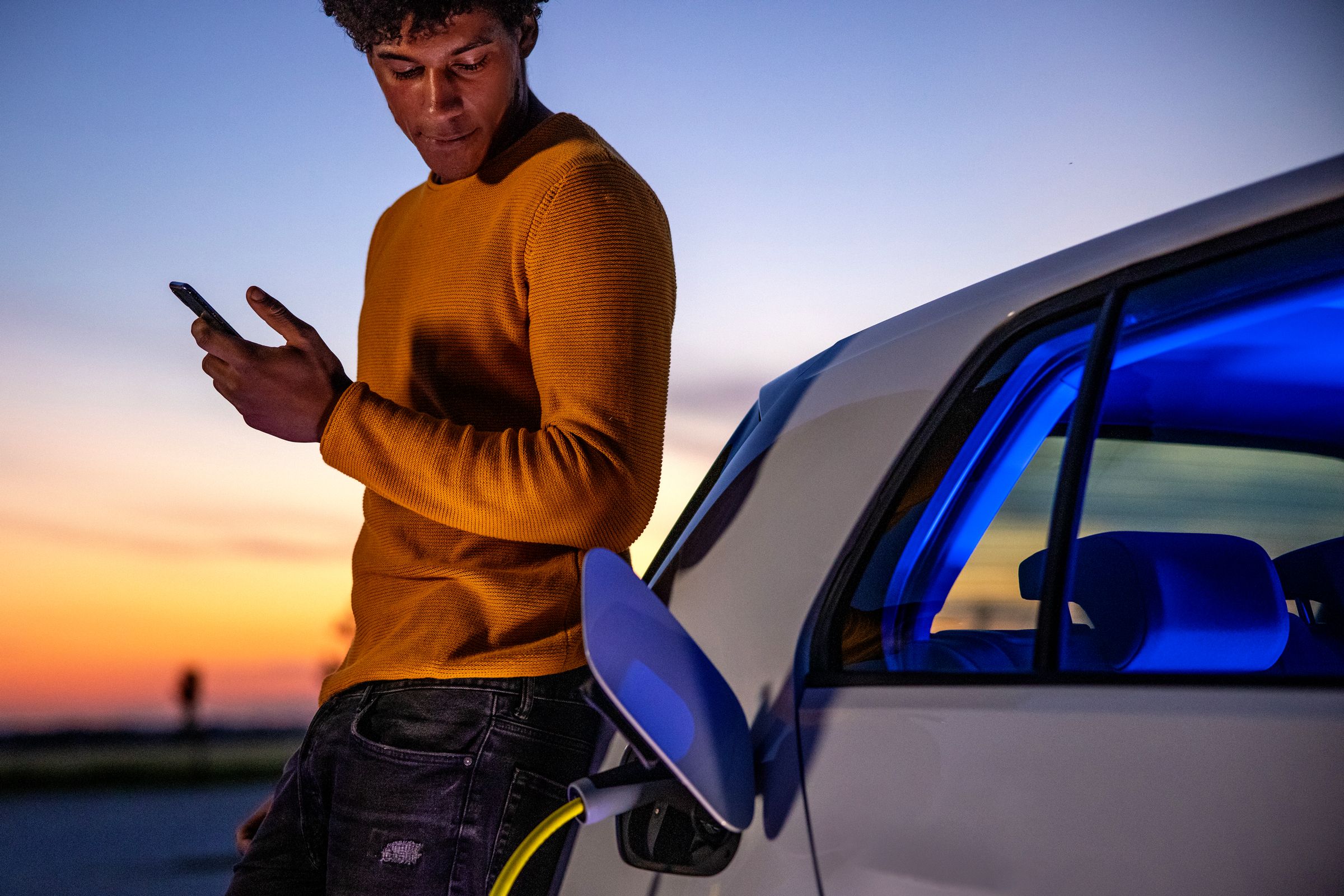 A person checking their smartphone next to an electric car that's charging, representing how apps make finding free EV charging at work or shopping centers easier