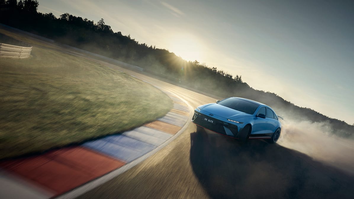A blue electric performance sedan drifts around a sunny racetrack corner with tire smoke, capturing the dynamic excitement of anticipated electric sports cars launching in 2027