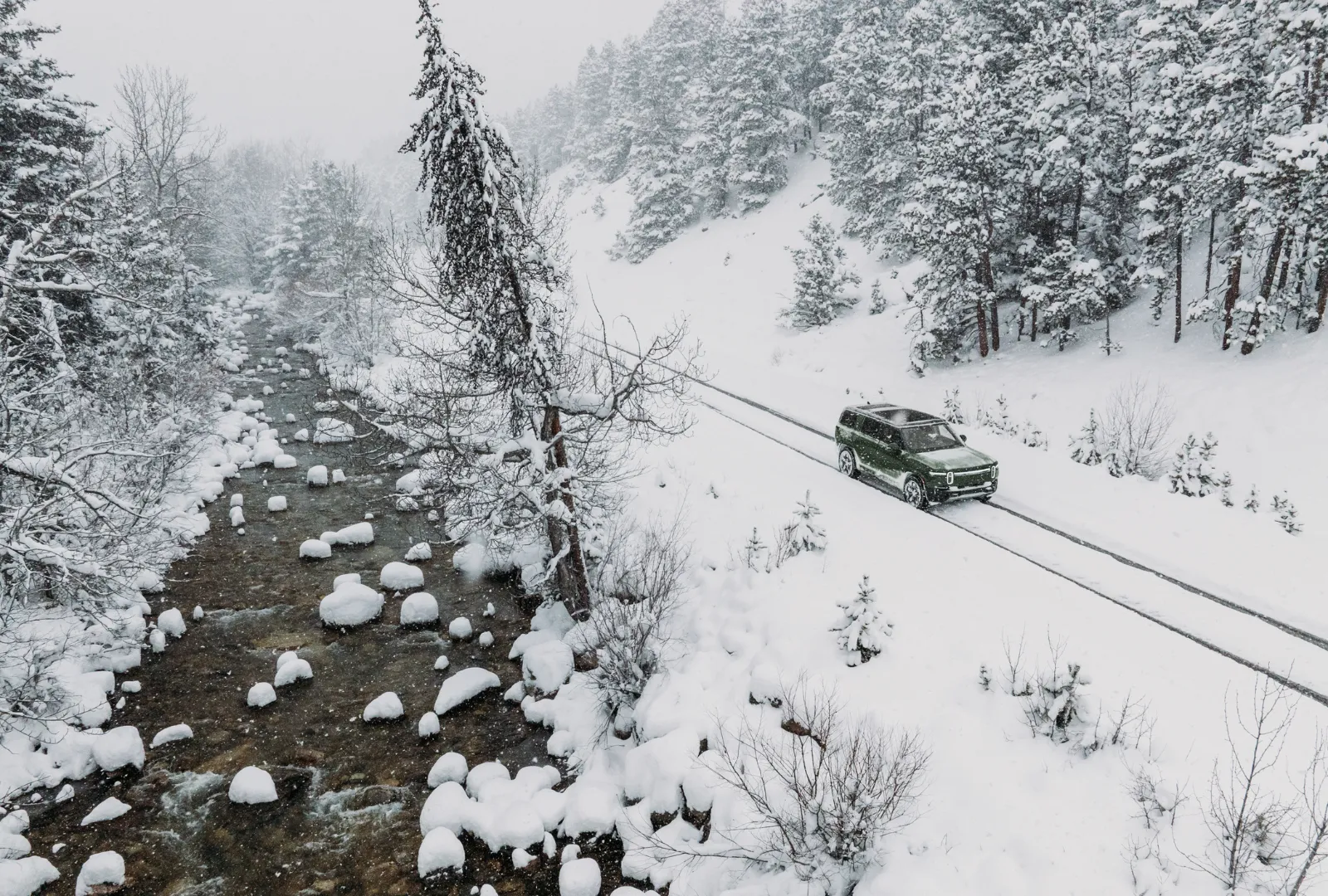 Electric SUV driving down a scenic snowy mountain road in daylight, capturing the real-world use of regenerative braking to recover energy on descents
