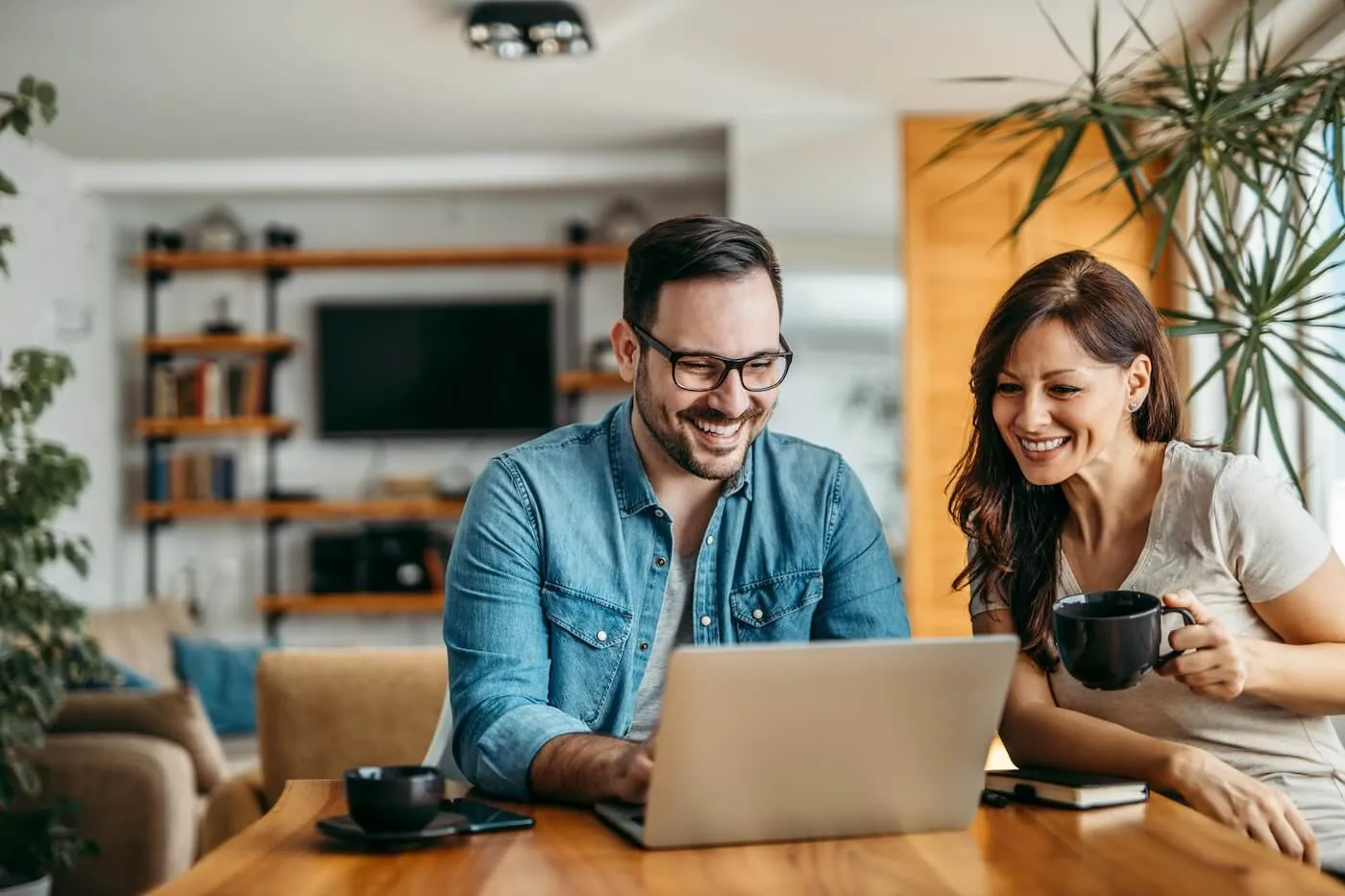 Happy couple reviewing auto loan options together on a laptop at home, planning their electric vehicle purchase with the best rates available