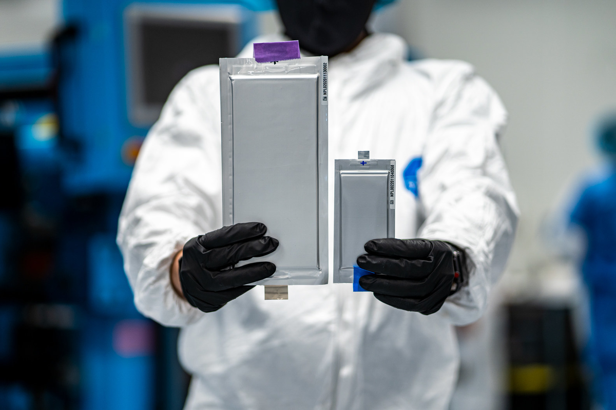 Researcher in a cleanroom carefully holding two solid-state battery prototypes side by side, showing real progress in next-gen battery development