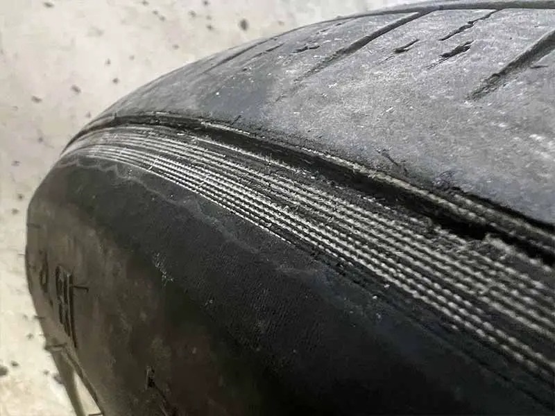 Real close-up photo of a severely worn tire with tread completely bald and cords showing, common with the quicker tire degradation many EV owners experience
