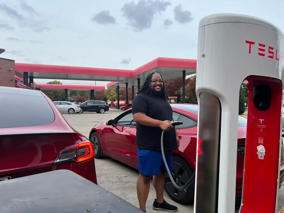 Person charging a red Tesla Model 3 at a public Supercharger station in natural daylight, real-life scene representing efficient charging for electric sedans like Tesla Model 3 vs Hyundai IONIQ 6