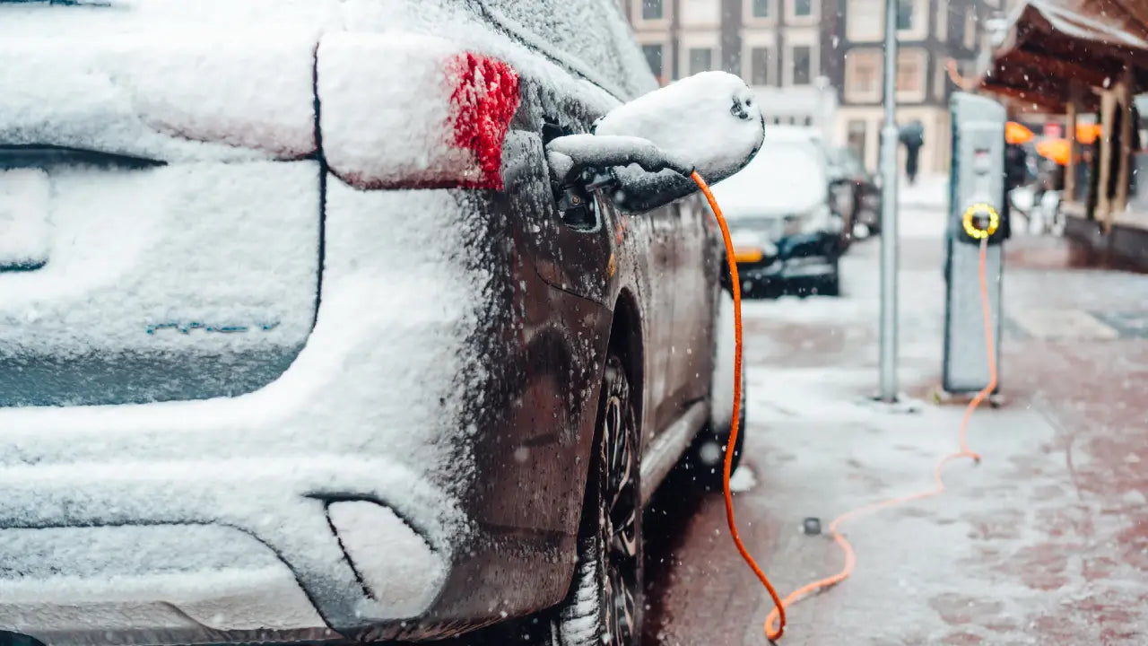 Frost-covered electric car connected to charger during active snowfall, ideal setup for preconditioning the battery while plugged in at home