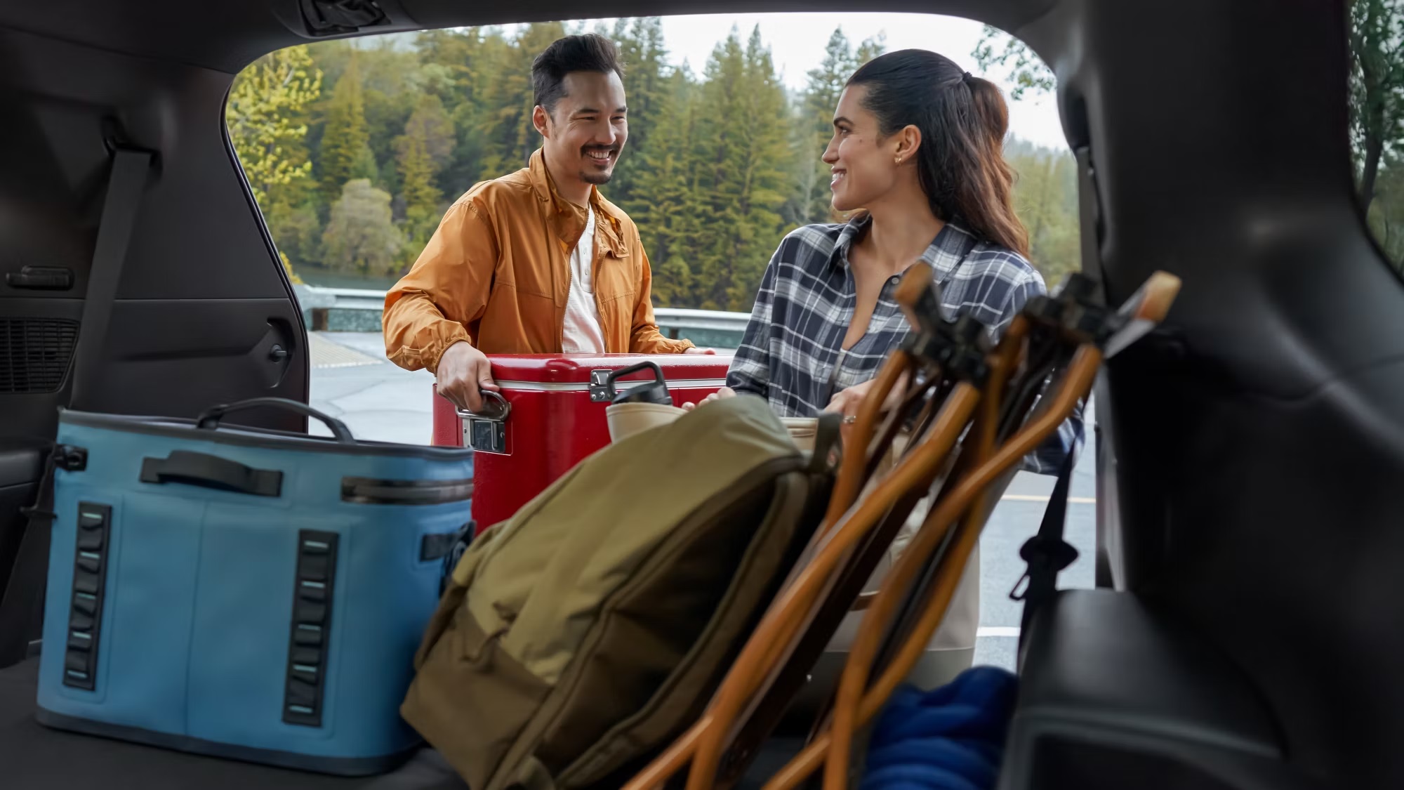 Open trunk of an SUV loaded with coolers, bags, and camping gear on a sunny day, representing how a portable EV charger fits easily into road trip packing for emergencies