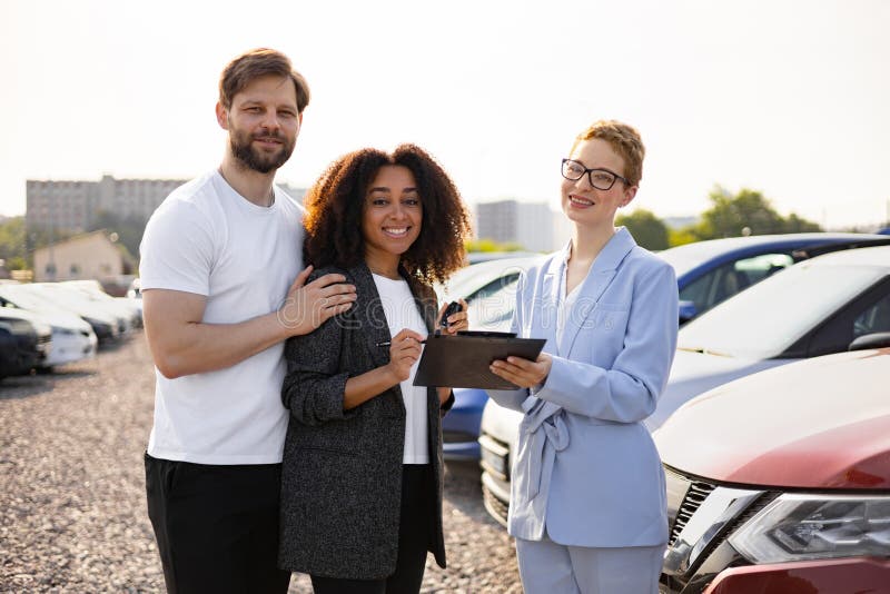 A diverse couple happily signing paperwork at a car dealership with a salesperson, excited about their new electric vehicle purchase qualifying for the 2026 federal EV tax credit claim