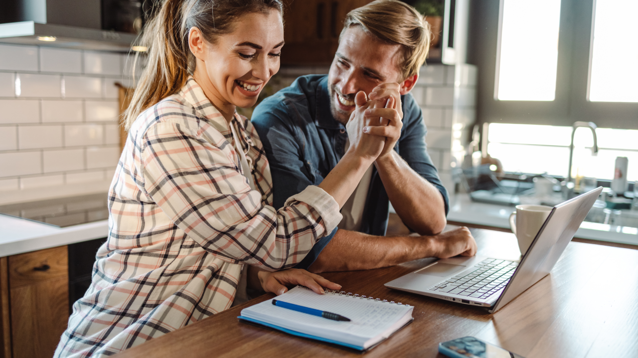 A happy couple at their kitchen table looking relieved and smiling while reviewing tax documents, celebrating a successful federal EV tax credit claim in 2026