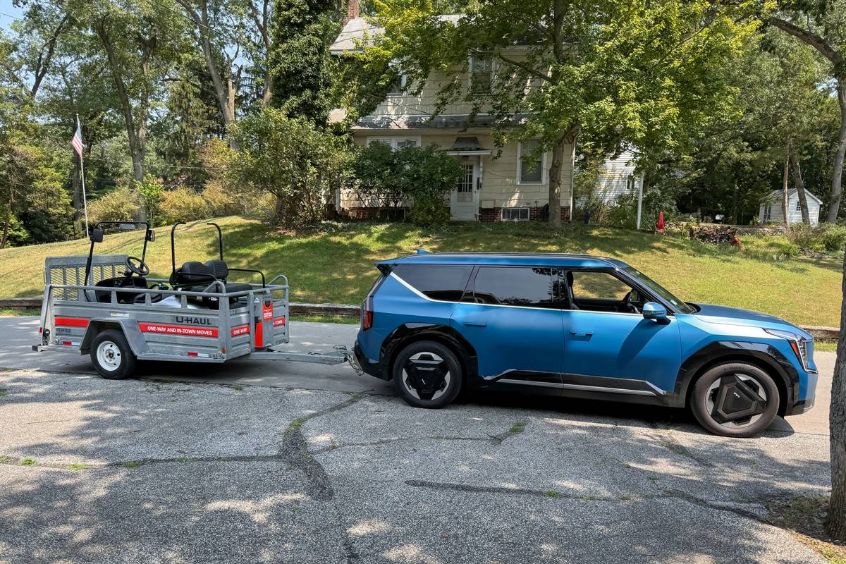 Blue Kia EV9 electric SUV hitched to a U-Haul trailer on a sunny day, proving that affordable electric SUVs for towing can handle real moving jobs with good range and family-friendly space.
